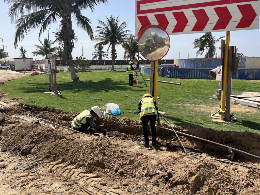 Crew laying irrigation pipe in a trench beside a finished lawn